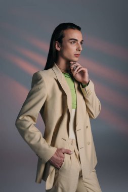 Trendy queer model in beige suit looking away on abstract background 