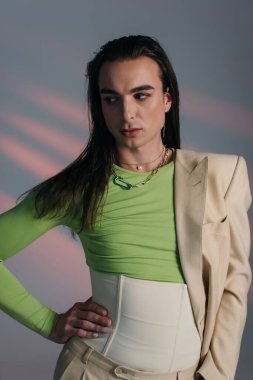 Brunette queer model in corset and jacket looking away on abstract background 