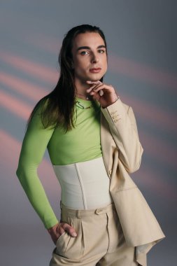 Trendy nonbinary model in suit looking at camera on abstract background 