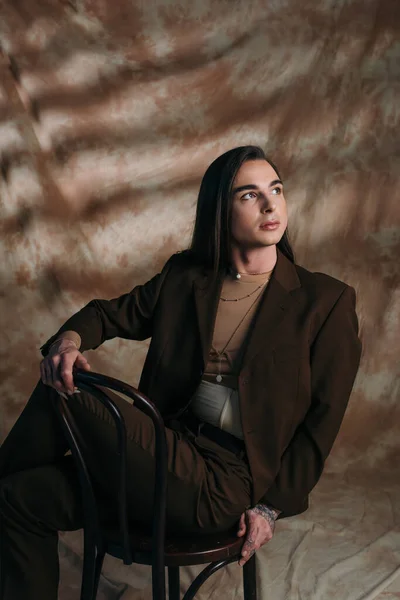 Trendy Nonbinary Person Looking Away While Sitting Chair Abstract Brown — Stockfoto