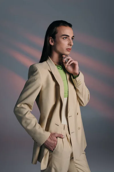 Trendy Queer Μοντέλο Μπεζ Κοστούμι Κοιτάζοντας Μακριά Αφηρημένο Φόντο — Φωτογραφία Αρχείου
