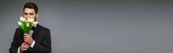 Γενειοφόρος Άνδρας Κομψό Σμόκιν Μυρίζοντας Φρέσκες Τουλίπες Που Απομονώνονται Γκρι — Φωτογραφία Αρχείου