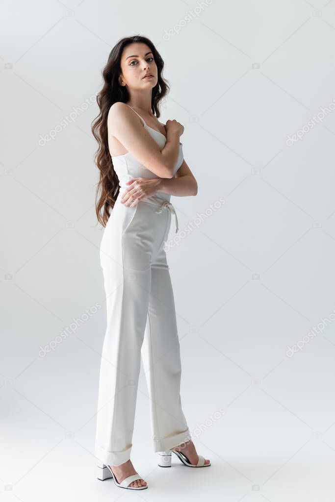 Full length of stylish long haired woman looking at camera on grey background