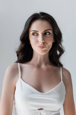 Portrait of sly woman in white top isolated on grey 