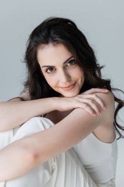 Portrait of smiling woman in white top looking at camera isolated on grey 