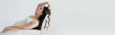 Side view of long haired model posing near chair isolated on grey, banner 