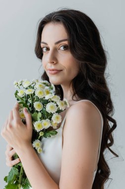 Portrait of long haired model holding flowers isolated on grey 