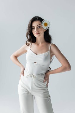 Woman in white clothes and with chamomile in hair standing isolated on grey 