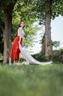 Smiling woman holding blanket near basket in park 