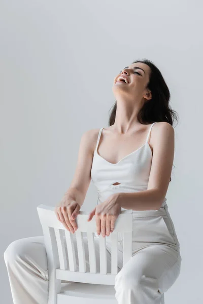 Positive Brunette Woman Laughing While Sitting Chair Isolated Grey — Zdjęcie stockowe