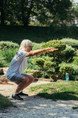 full length of cheerful senior man with grey hair working out with outstretched hands outside