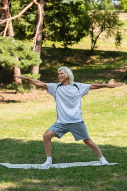 full length of cheerful senior man with grey hair smiling and working out with outstretched hands in park