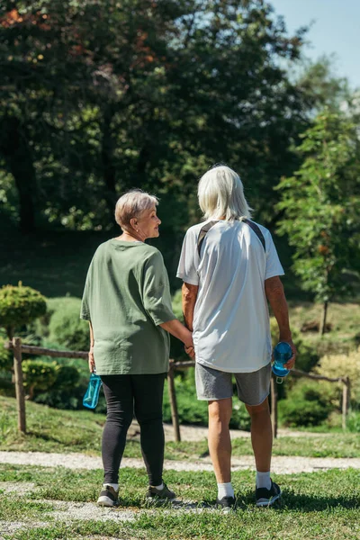 Happy Retired Woman Sportswear Looking Husband Sport Bottle Holding Hands — Stockfoto