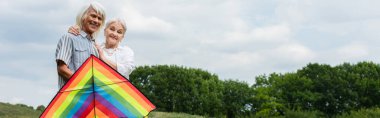 happy senior woman in casual clothes hugging husband in glasses standing with kite, banner