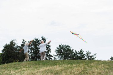senior couple in casual clothes playing with kite on green hill 