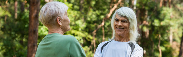 joyful senior couple in sportswear looking at each other in green park, banner