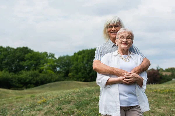 Cheerful Senior Man Glasses Hugging Wife Grey Hair Standing Park — Stock Photo, Image