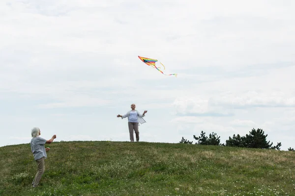 Cheerful Senior Woman Casual Clothes Looking Kite Husband Green Hill — Fotografia de Stock