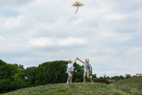 Cheerful Senior Couple Casual Clothes Holding Hands While Playing Kite — Stock Photo, Image