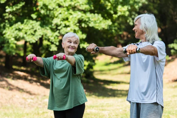 Positive Retired Couple Sportswear Exercising Dumbbells Green Park — 图库照片