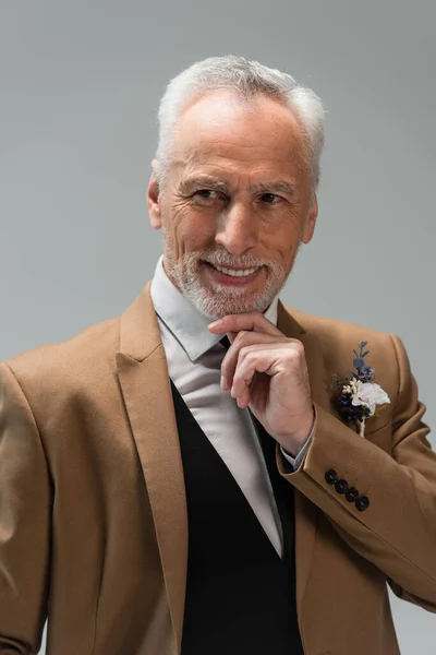 cheerful middle aged groom in suit with floral boutonniere isolated on grey