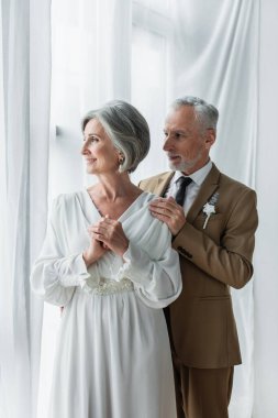 bearded middle aged groom in suit touching shoulder of happy bride in white dress