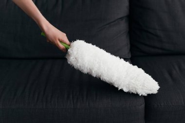 partial view of woman cleaning couch with dust brush