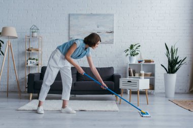 full length of woman cleaning floor with mop in modern living room