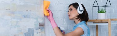 young brunette woman in wireless headphones wiping picture with rag, banner