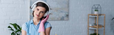 smiling housewife in rubber glove and wireless headphones looking at camera, banner