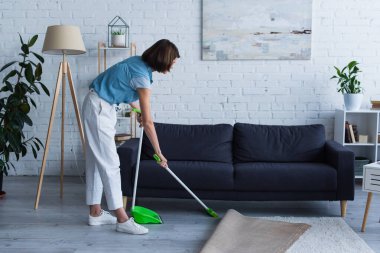 side view of woman sweeping floor near sofa in living room