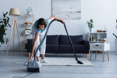 Woman switching on vacuum cleaner in living room 