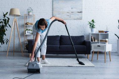Woman switching on vacuum cleaner in living room  clipart