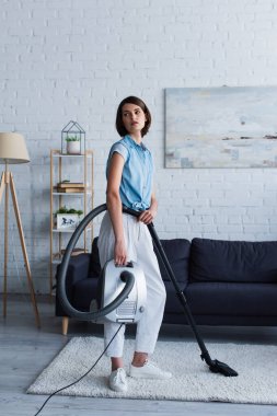 Young woman holding vacuum cleaner on carpet in living room 