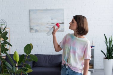 Side view of woman spraying air freshener in living room  