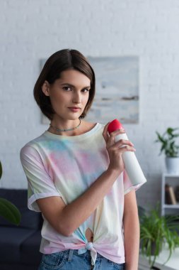 Young woman looking at camera and holding air freshener at home 