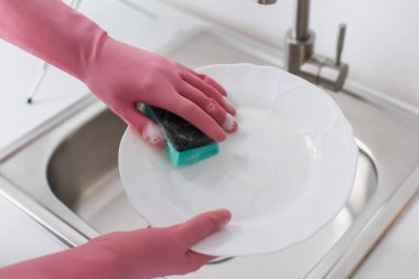 Cropped view of woman in rubber gloves washing plate in kitchen 