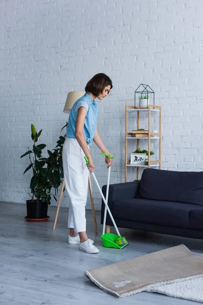 full length of young woman sweeping floor with broom in living room