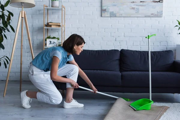 side view of housewife sweeping floor under couch in living room