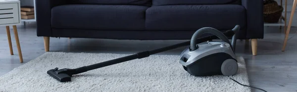 Vacuum cleaner on carpet near couch in living room, banner