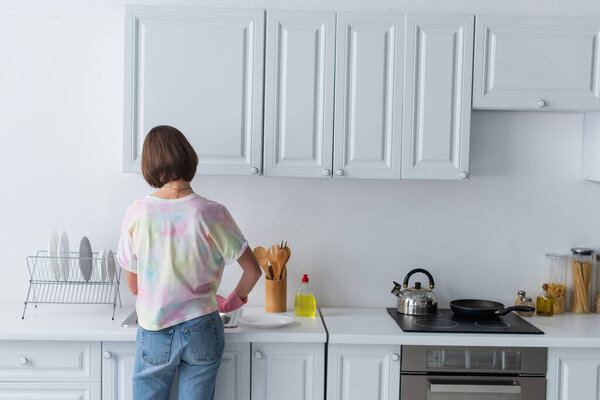 Back view of woman standing near plates and sink in kitchen 