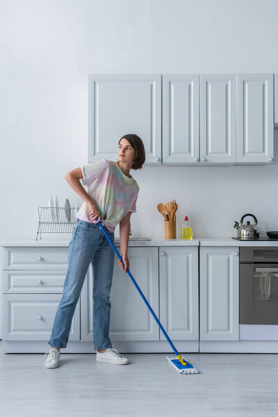 Young woman cleaning floor with mop in kitchen 