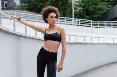 sportive african american woman with curly hair looking away on stadium