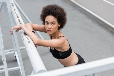 high angle view of young african american sportswoman leaning on fence and looking at camera