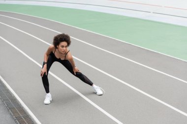 young african american woman warming up on stadium while doing side lunge exercise