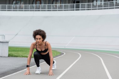 young african american jogger standing in low start pose on track