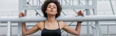 pretty and sportive african american woman looking at camera near stadium fence, banner