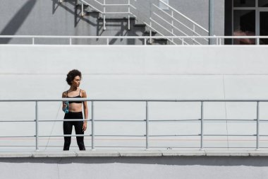 young african american sportswoman standing with sports bottle on city stadium