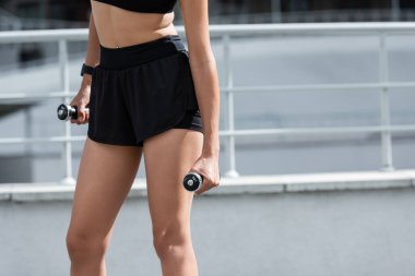 Cropped view of fit african american sportswoman holding dumbbells on stadium 