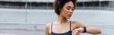 Young african american sportswoman looking at smart watch on stadium, banner 